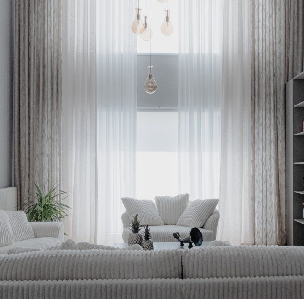 A minimalist living room with soft white sofas and large curtains, creating a cozy atmosphere.
