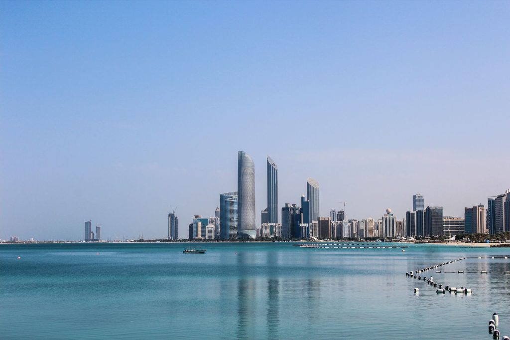 Stunning view of the Abu Dhabi skyline reflecting in the calm Gulf waters on a sunny day.